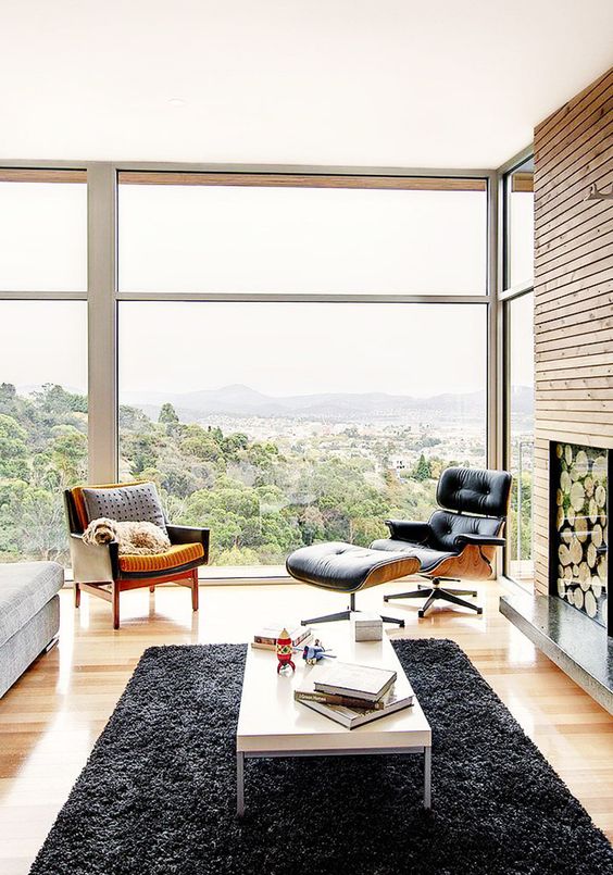 a stylish farmhouse space with a non-working fireplace with wood, an Eames lounger and ottoman, a black chair, a grey sofa, a low coffee table