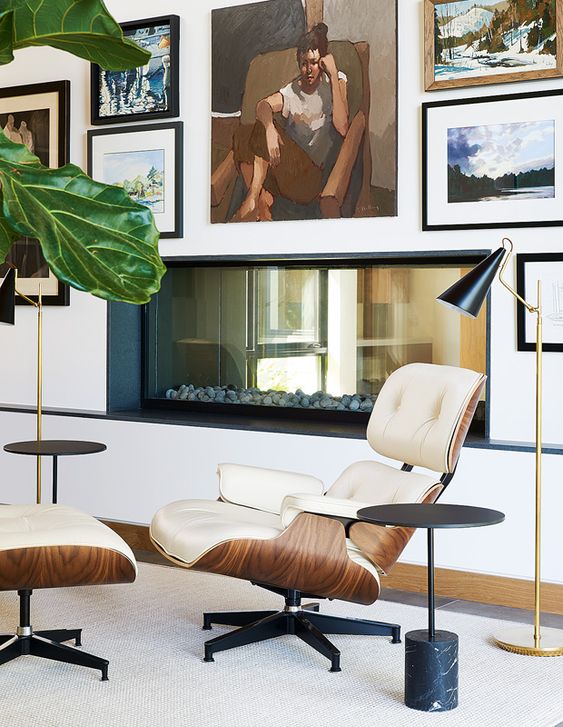 a stylish fireplace nook with a built-in fireplace, a creamy lounger and an ottoman, black and gold floor lamps and black side tables, a beautiful gallery wall