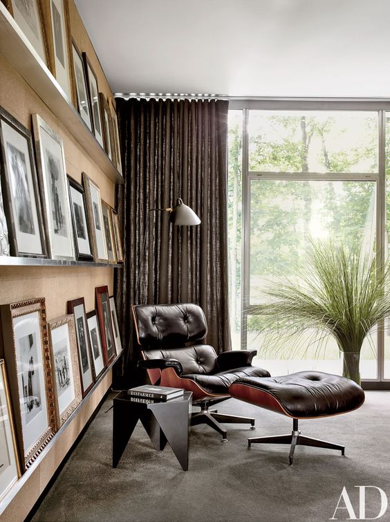 a stylish mid-century modern nook with a black Eames lounger and ottoman, a black side table and three ledges presenting a gallery wall