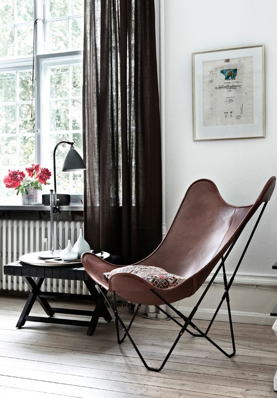 a stylish modern sitting nook with a brown butterfly chair, a side table with vases and a lamp plus brown curtains