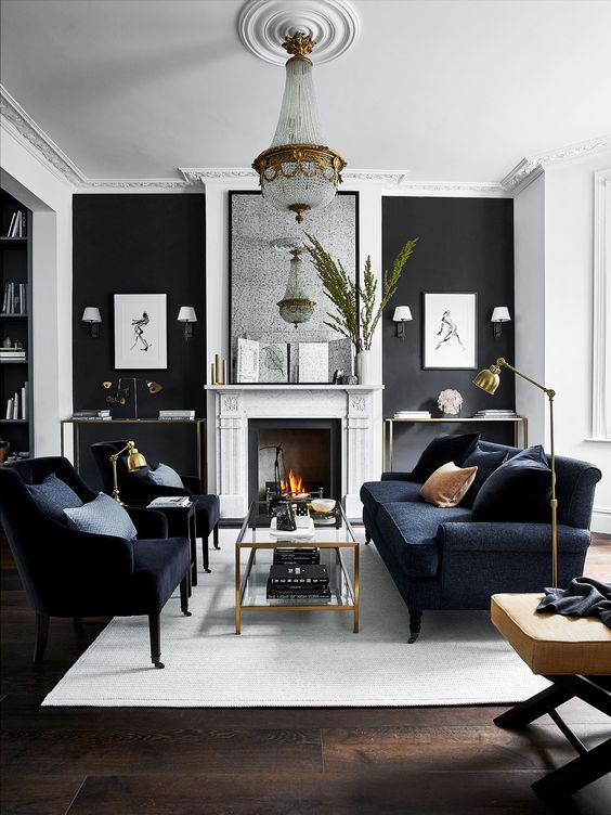 a stylish monochromatic living room with a black accent wall, a fireplace, two consoles, a black sofa and chairs, a tiered glass coffee table