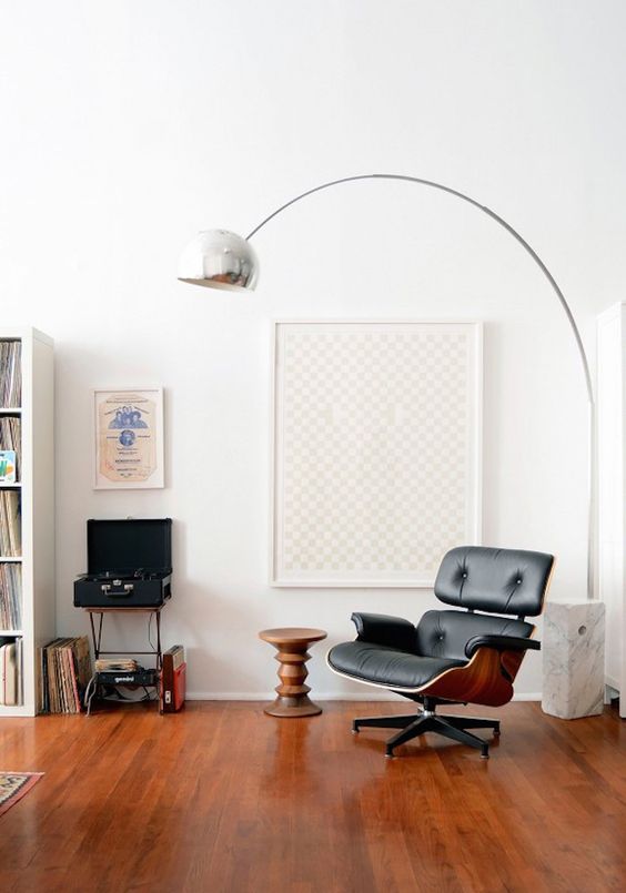 a stylish nook with a black Eames lounger, a side table, a polished metal floor lamp and some art and books