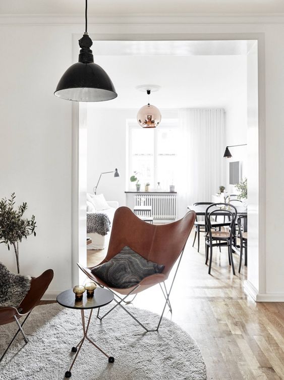 a stylish sitting nook with a side table, brown leather butterfly chairs, a round rug and a black pendant lamp