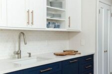 a stylish two-tone kitchen with navy and white cabinets, shaker and open ones, white stone countertops, a white tile backsplash and brass fixtures