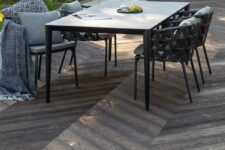 a terrace clad with antique oak composite decking, with a modern dining table and black chairs plus grey upholstery