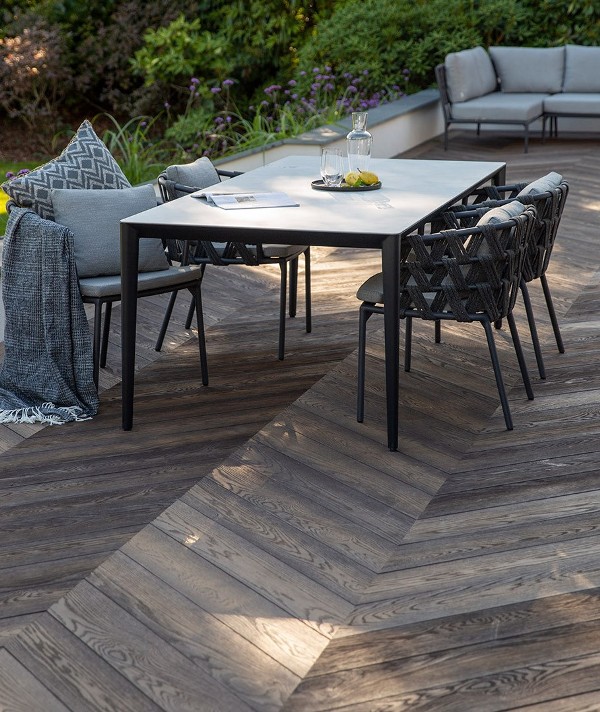 a terrace clad with antique oak composite decking, with a modern dining table and black chairs plus grey upholstery