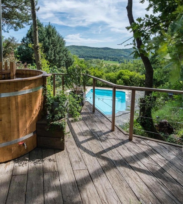 a terrace with a hot tub clad with weathered oak millboard, with potted greenery and a view of the poll below