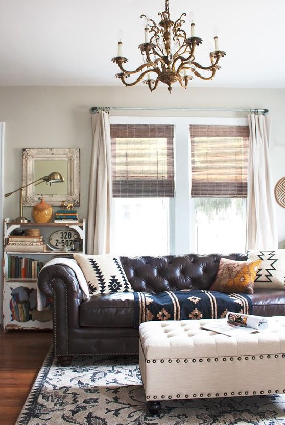 a vintage and shabby chic living room with a brown leather Chesterfield sofa, a matching white ottoman and a refined gilded chandelier