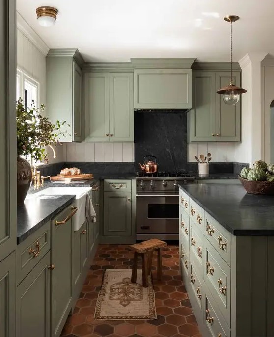 a vintage green kitchen with shaker style cabinets, black soapstone countertops and a backsplash, white beadboard walls and pendant lamps