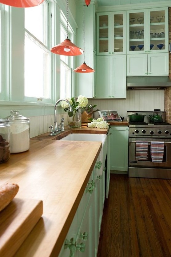 a vintage-inspired mint green kitchen with butcherblock countertops, pink pendant lamps and a white beadboard backsplash