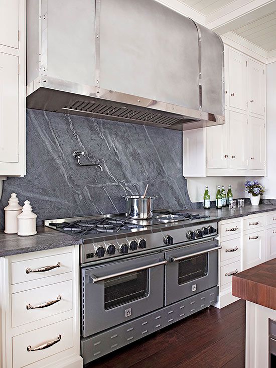 a vintage white kitchen with flat panel cabinets, a grey soapstone backsplash and countertops, stainless steel appliances