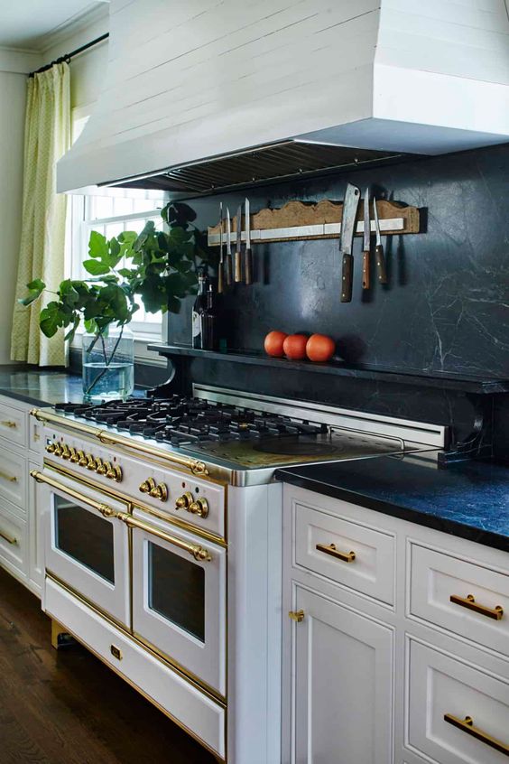 a vintage white kitchen with shaker cabinets, black soapstone countertops and a backsplash, gold touches and fixtures
