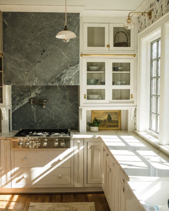 a vintage white kitchen with usual and shaker cabinets, neutral countertops, a grey soapstone backsplash and a hood is a stylish idea