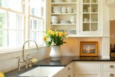 a warm-colored farmhouse kitchen with shaker and open cabinets, black countertops, a white tile backsplash and stainless steel fixtures