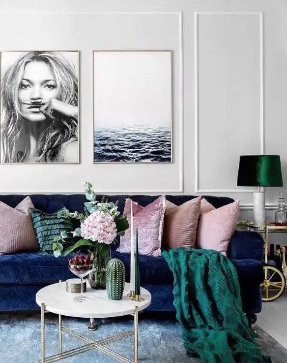 a welcoming living room with a navy sofa, pink pillows and a green blanket, a lamp with an emerald lampshade, a round coffee table and some blooms