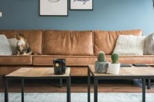 a welcoming living room with blue walls, a gallery wall, wooden tables and a sectional brown leather sofa