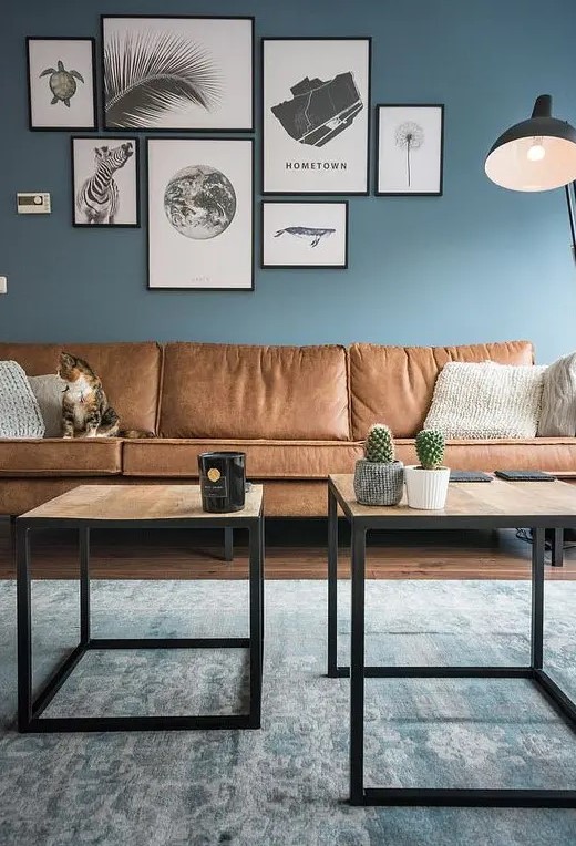 a welcoming living room with blue walls, a gallery wall, wooden tables and a sectional brown leather sofa