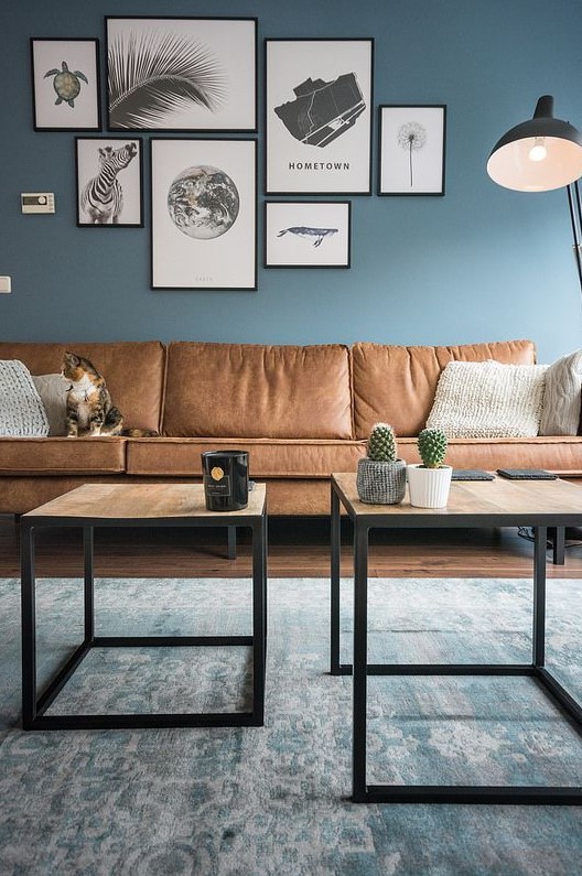 a welcoming living room with blue walls, a gallery wall, wooden tables and a sectional brown leather sofa