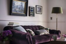 a welcoming living room with lilac walls, a refined purple velvet sofa, a lilac rug, a vintage gallery wall, a green floor lamp and a dark stained table