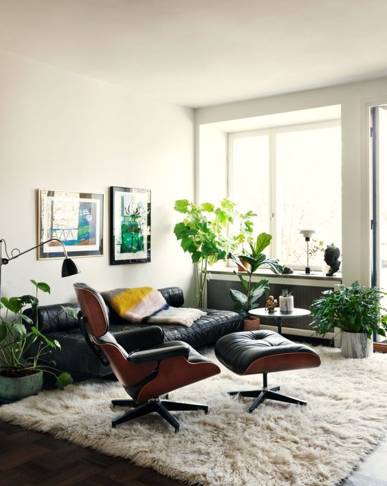 a welcoming mid-century modern living room with a black leather sofa, a black Eames lounger and ottoman, potted greenery and a fluffy rug