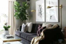 a welcoming modern living room with grey walls, a black sofa, potted plants, a clear acrylic coffee table and printed pillows