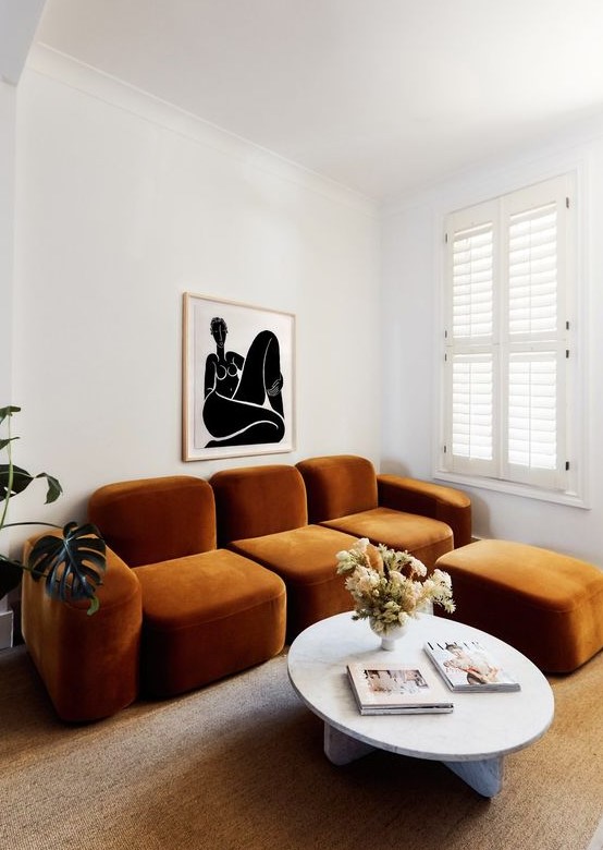 a whimsical living room with a quirky rust-colored sofa and an ottoman, a round table and a bold artwork