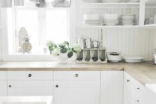 a white cottage kitchen with closed and open storage cabinets, butcherblock countertops, a kitchen island and railing with cookware