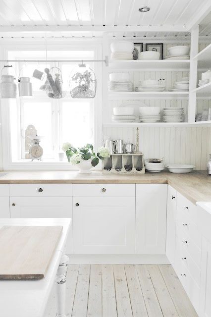 a white cottage kitchen with closed and open storage cabinets, butcherblock countertops, a kitchen island and railing with cookware