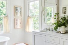 a white farmhouse bathroom with marble hex tiles, double-hung windows, an oval tub, a large vanity and a window cabinet