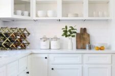 a white farmhouse kitchen with open upper cabinets, a white subway tile backsplash, stone countertops and a wine bottle stand