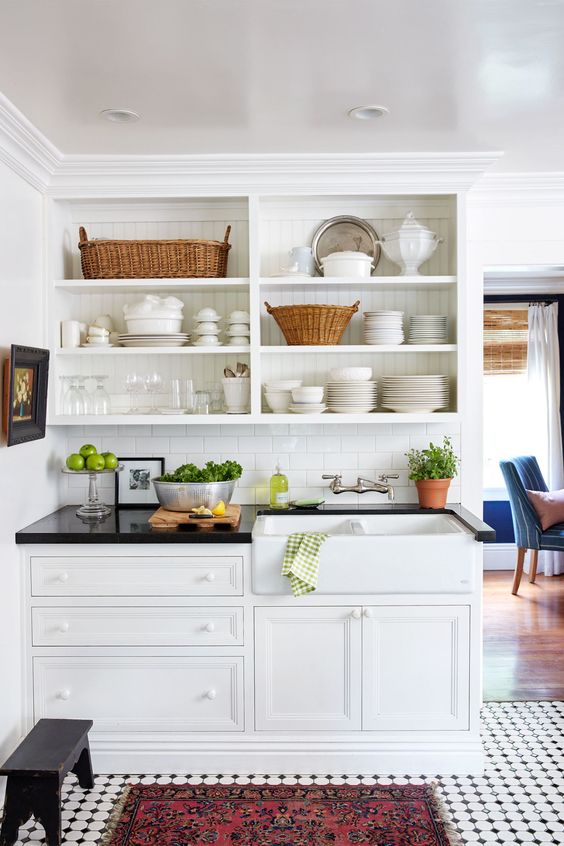 a white farmhouse kitchen with shaker and open cabinets, black countertops and potted plants and beautiful decor