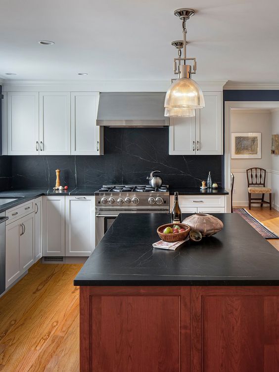 a white farmhouse kitchen with shaker cabients, a black soapstone backsplash and countertops, a stained kitchen island and chic pendant lamps