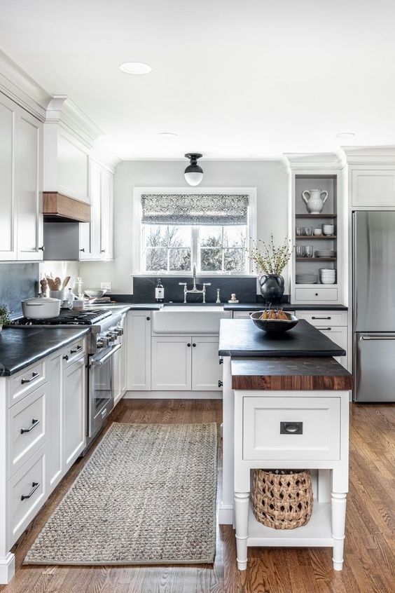 a white farmhouse kitchen with shaker cabinets, black soapstone countertops and a backsplash, touches of stained wood