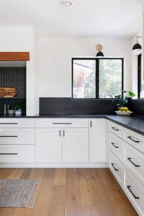 a white farmhouse kitchen with shaker cabinets, black soapstone countertops and a backsplasj, skinny tiles and black fixtures