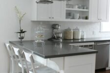 a white kitchen with shaker and open cabinets, black countertops, metal pendant lamps and a potted flower is cool and chic