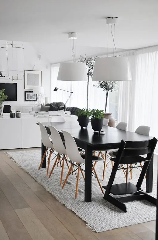an airy Scandinavian dining room with a black table, white Eames chairs, white pendant lamps and a pretty and very simple rug