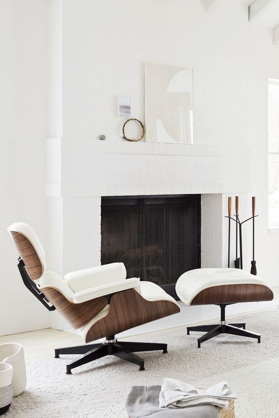 an airy and cozy fireplace nook with a white Eames lounge chair and an ottoman, with some decor on the mantel
