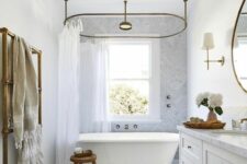 an airy bathroom with a double-hung window, a large vanity, an oval clawfoot bathtub and a marble herringbone tile floor