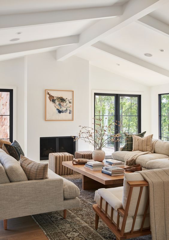 an airy living room with grey sofas, a low coffee table, a creamy chair and striped poufs plus a fireplace