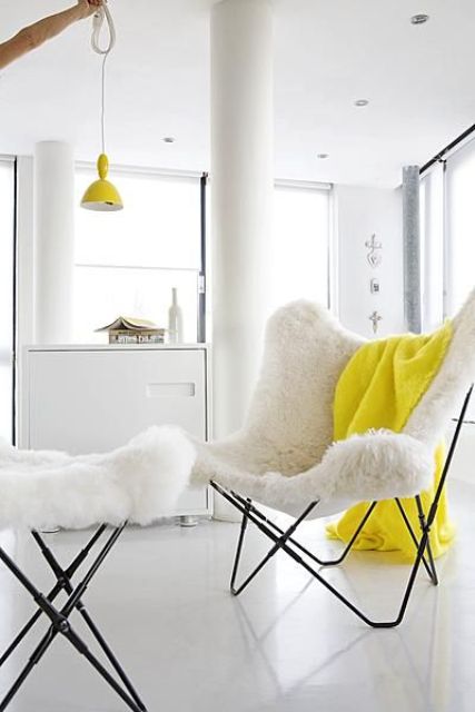 an airy nook with a white faux fur butterfly chair and a footrest, a bold yellow blanket and a yellow pendant lamp