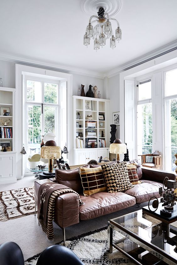 an amazing boho living room done in white, with bookcases and decor, made cozier with a brown leather sofa and a glass coffee table