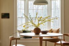 an earthy dining room with a bay window with a window seat, a round table and mid-century modern chairs, a pendant lamp