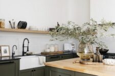 an earthy kitchen with dark green shaker cabinets and a matching kitchen island, black and butcherblock countertops, an open shelf and black fixtures