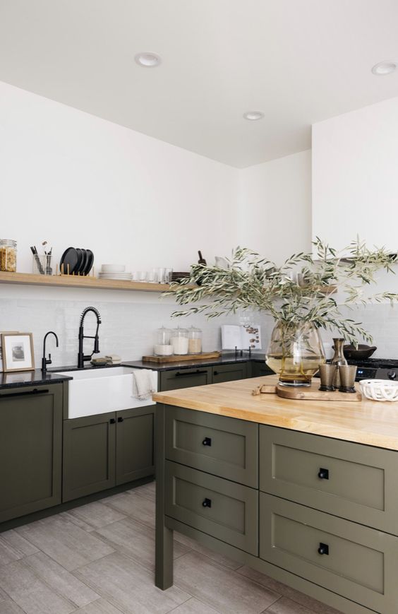 an earthy kitchen with dark green shaker cabinets and a matching kitchen island, black and butcherblock countertops, an open shelf and black fixtures