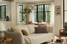 an earthy living room with a neutral sofa, a green chair, a low coffee table and a side one, a rough wooden beam