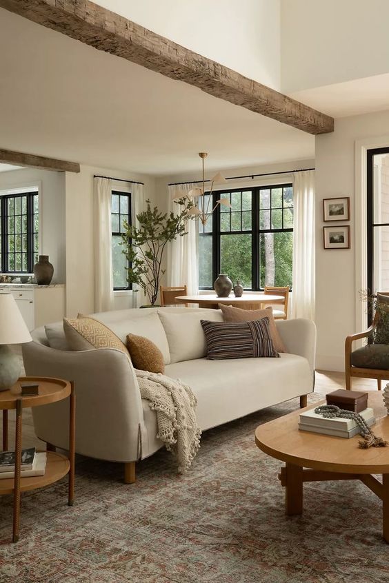 an earthy living room with a neutral sofa, a green chair, a low coffee table and a side one, a rough wooden beam