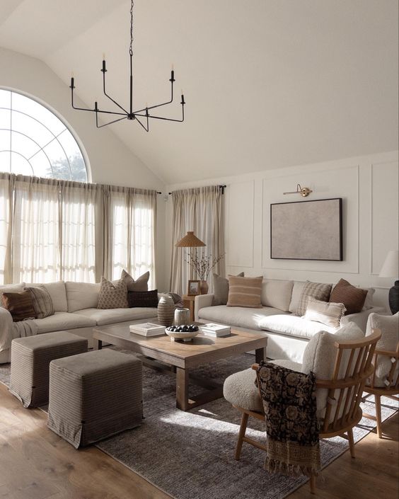 an earthy living room with creamy sofas, a low coffee table, taupe poufs, creamy chairs and printed pillows