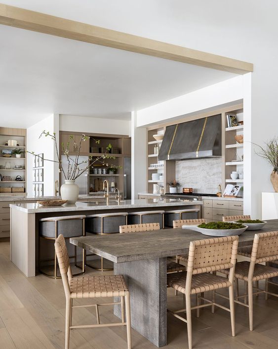 an earthy open layout with light colored cabinets, a large metal hood, a kitchen island and grey stools and a dining zone