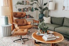 an earthy tone living room with a grey sofa, a tan Eames lounger and ottoman, a round coffee table, wall shelves and a potted plant