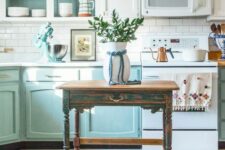 an eclectic kitchen with white and light blue cabinets, a white subway tile backsplash, open cabinets and a vintage table on casters